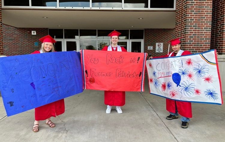 high school students wearing red graduation caps and gowns holding red, white and blue signs that say CONGRATS, You rock it former Patriots