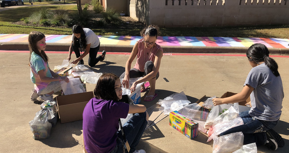 middle school students sitting in parking lot with paints to decorate the sidewalk