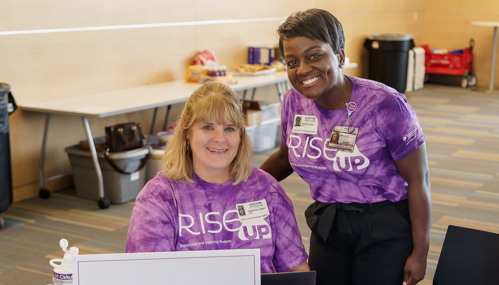 two women wearing purple tie-dyed shirts sit at a table