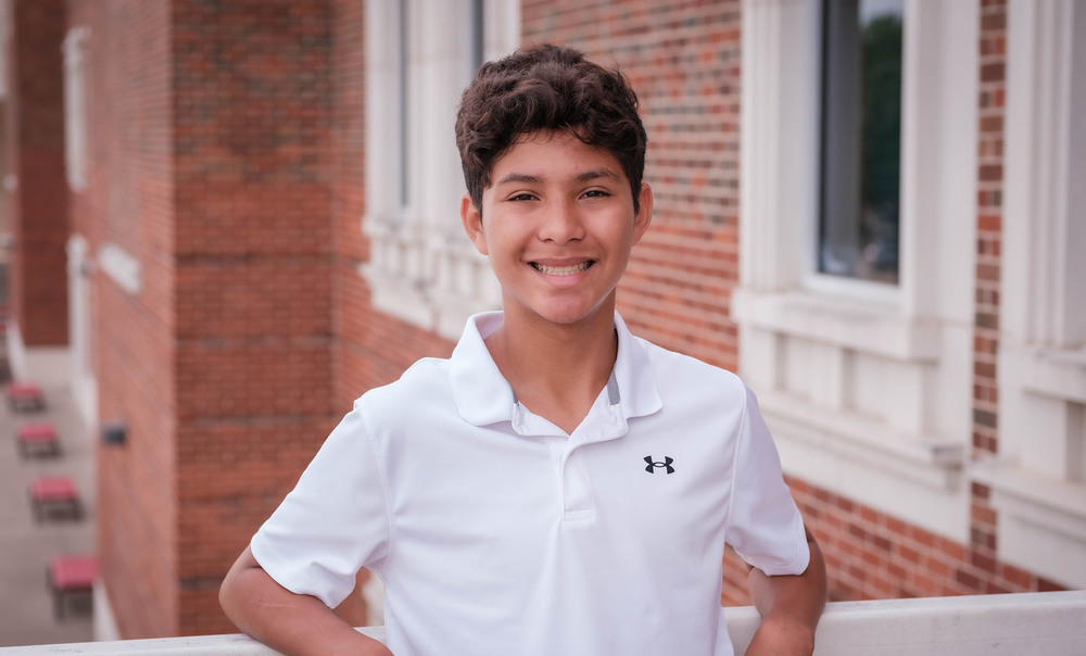 middle school age male wearing a white polo shirt smiles at the camera