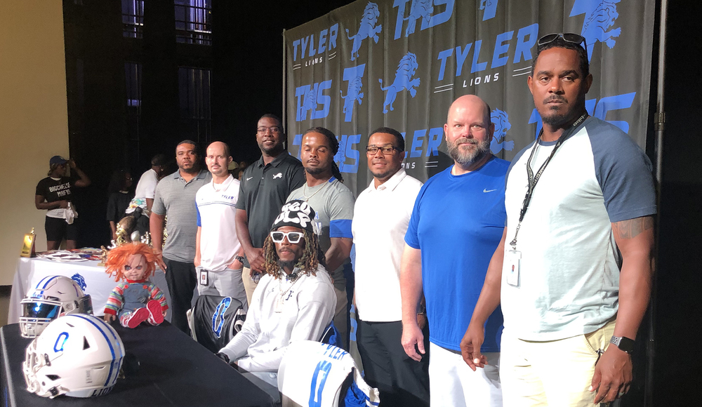 men standing behind African American football player for signing day
