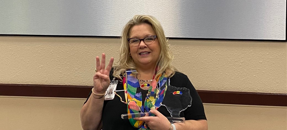 Sandy Newton holding up TAEA award & three fingers