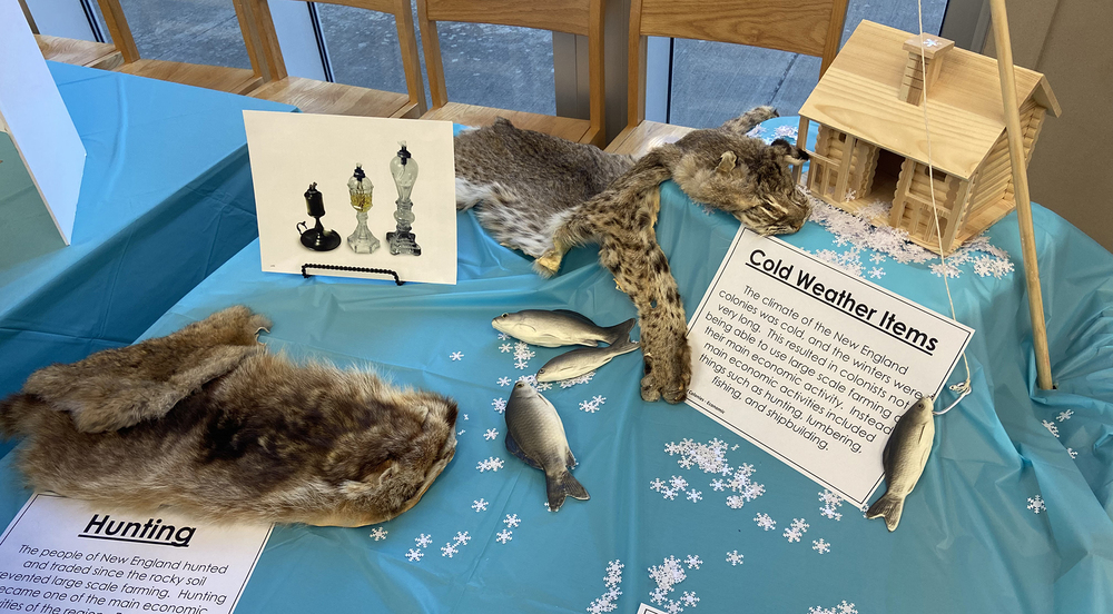 table with blue tablecloth on it. fur felts and fake fish lay on the table with a replica of a log cabin