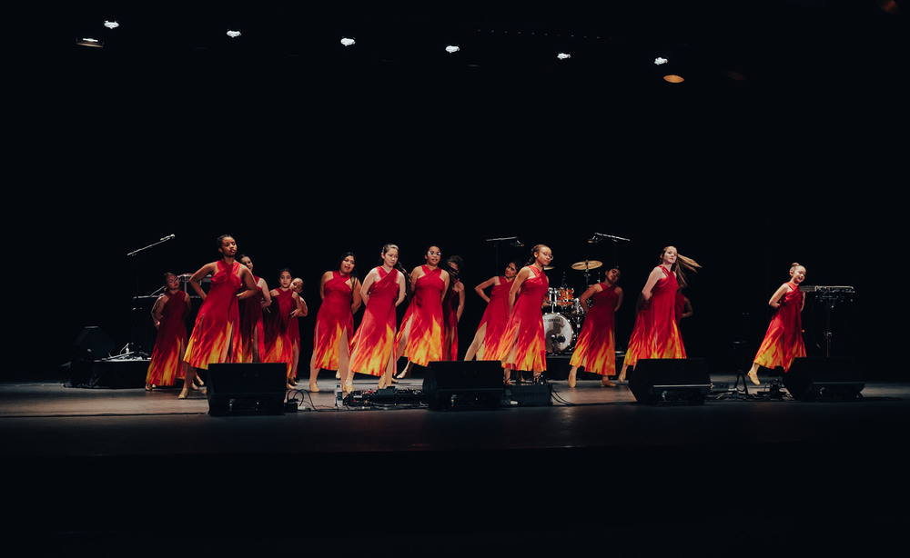 dancers wearing orange and red dresses perform on stage
