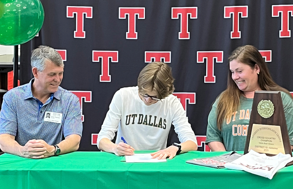 high school male sitting between his mom and dad as he signs a letter of intent to run cross country for UT Dallas