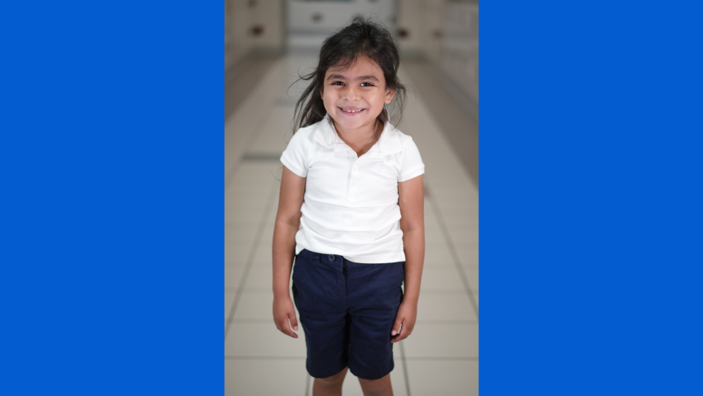 young Hispanic female wearing white polo and navy shorts smiling at the camera