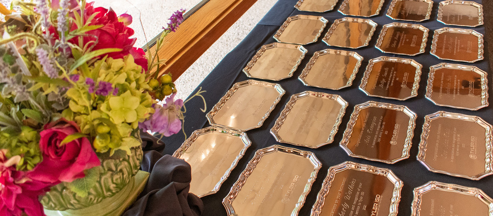 bright colored flowers in a vase on a table lined with gold trays engraved with retiree names