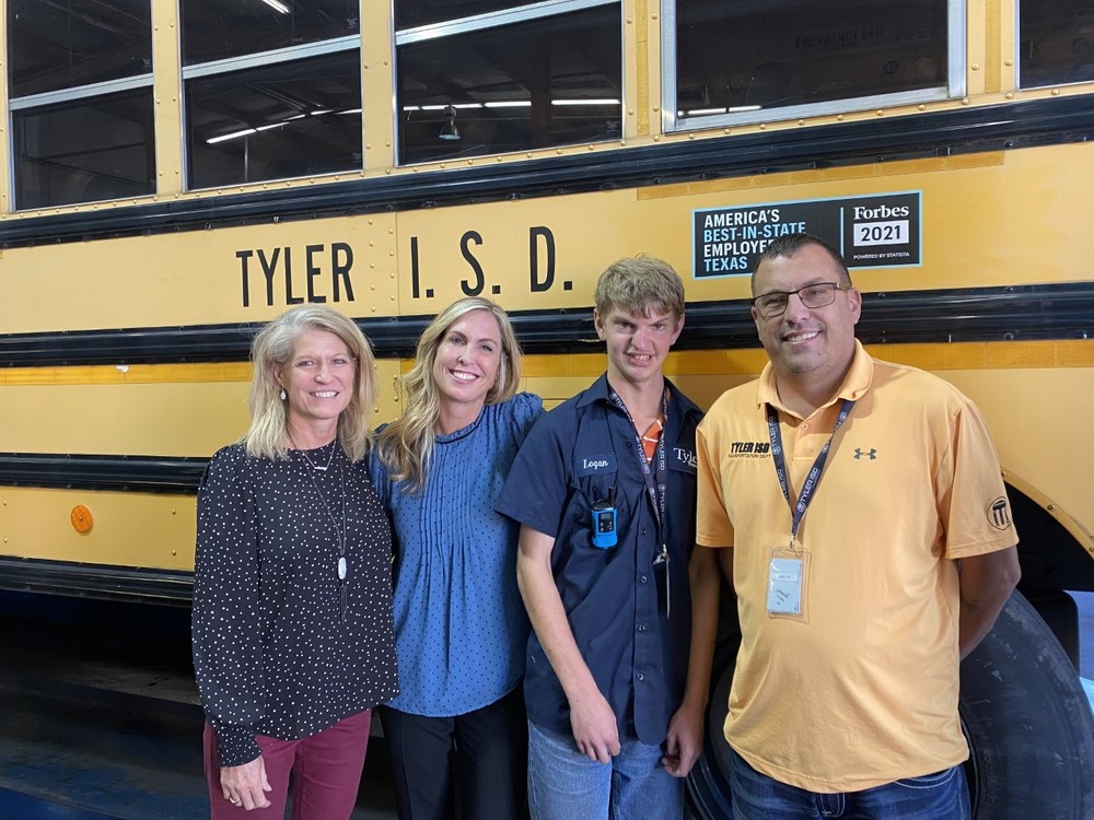 two women and two men stand beside each other in front of a school bus