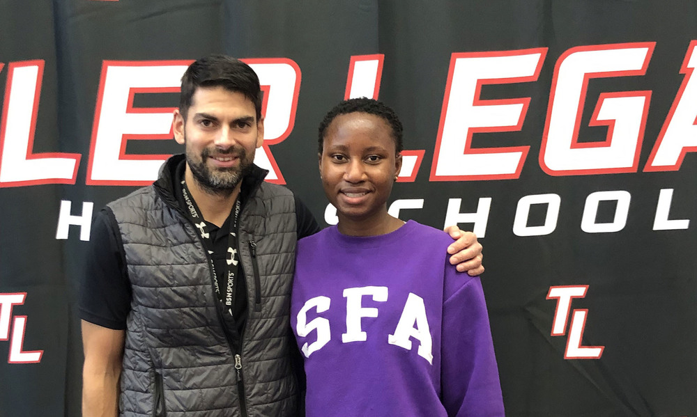 man with dark hair and beard wearing a gray vest stands next to teenage girl wearing a purple SFA sweatshirt