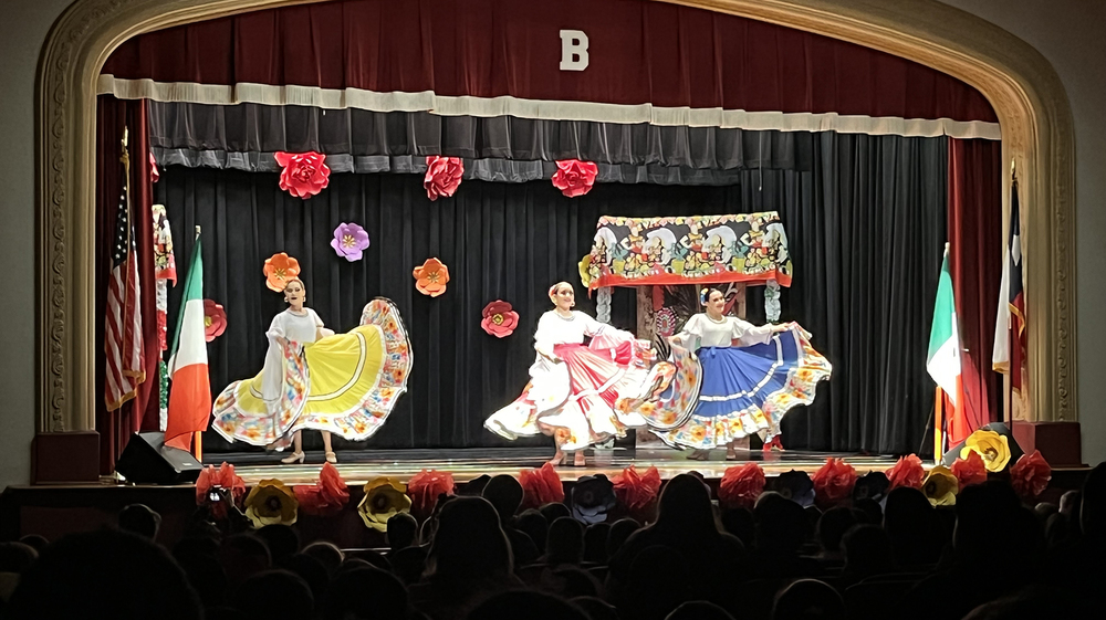 Folklorico dancers on stage in traditional costumes - yellow, red, blue long skirts