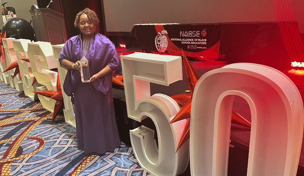 African American woman wearing a long purple dress holds an award