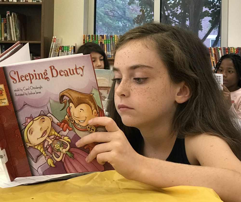 girl reading Sleeping Beauty book with other students in the background reading