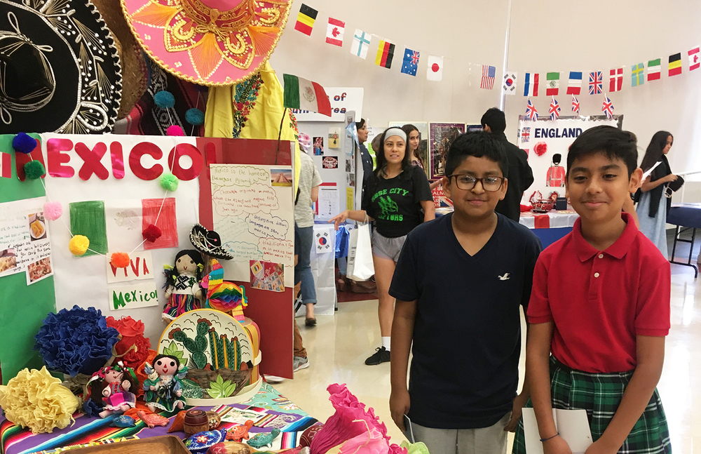 two middle school children stand next to a table decorated with cultural items from Mexico
