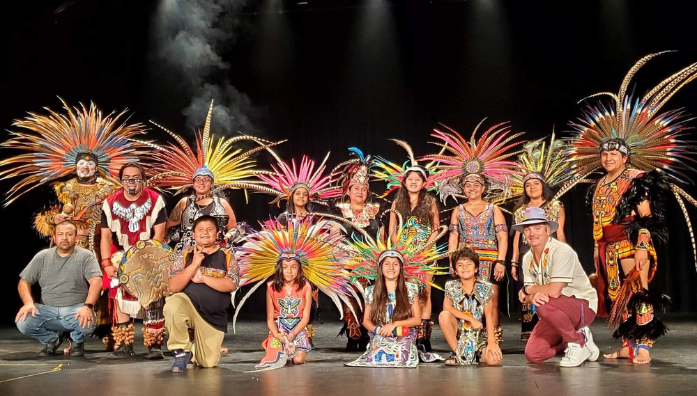 children on stage wearing brightly colored dresses and headdresses with bright feathers