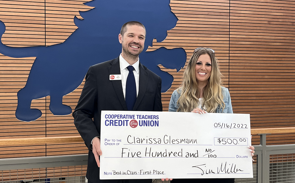 man in suit stands next to female holding giant check for $500
