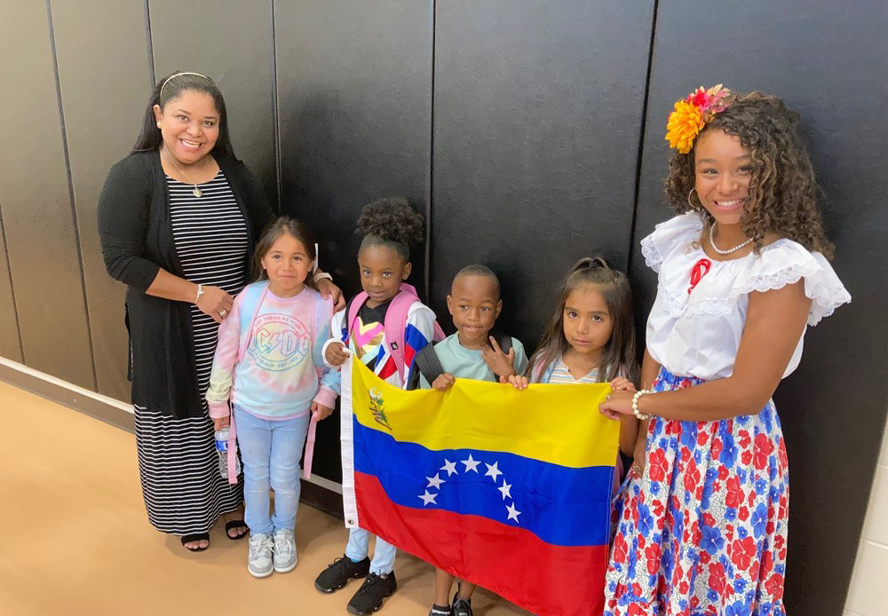 two women stand with four elementary age children between them holding a Venezuela flag