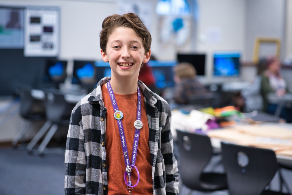 middle school age male student wearing an orange t-shirt with a black and white unbuttoned flannel shirt over it. he has a medal hanging around his neck with a purple ribbon