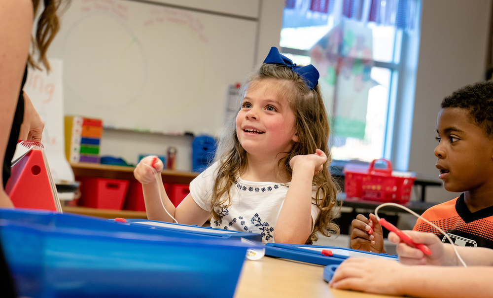 preschool age girl with long blonde hair and a blue bow, African American preschool boy - both sitting at a table