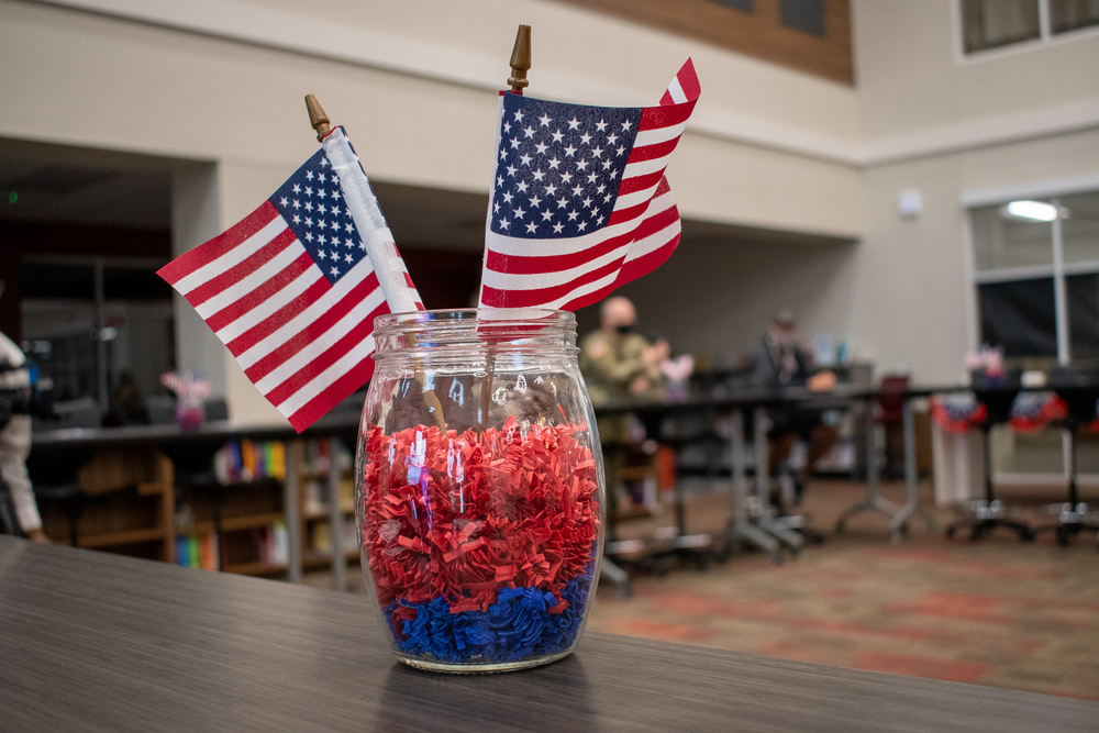 glass jar with red and blue confetti inside. two American flags sticking out the top.