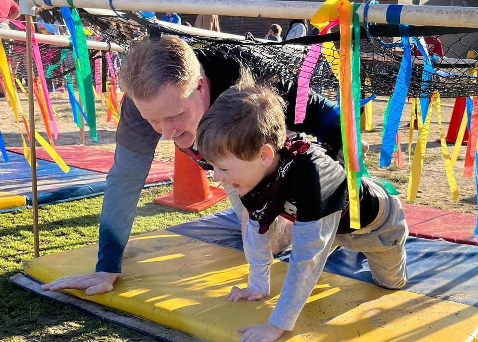 dad and son crawling under bar with ribbons hanging down