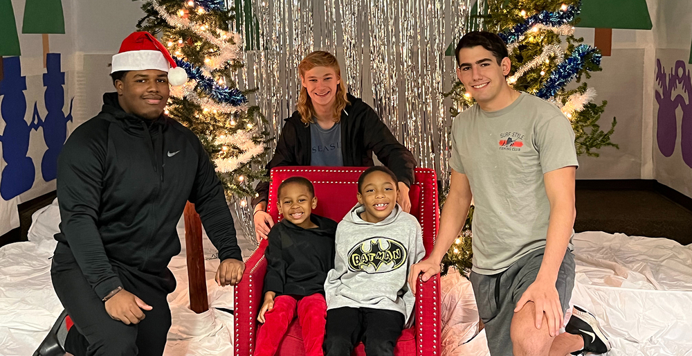 Legacy football players sitting with two elementary age children in front of a Christmas tree