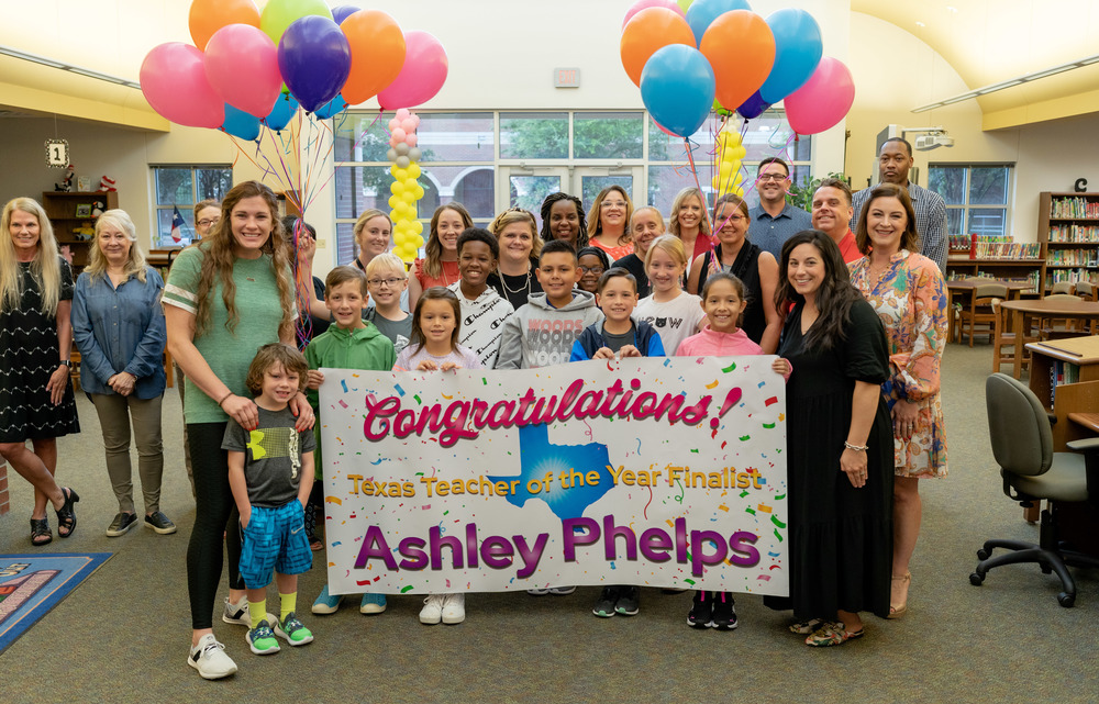 Congratulations Texas Teacher of the Year Finalist, Ashley Phelps. Phelps standing next to a banner, surround by students and faculty with balloon bouquets