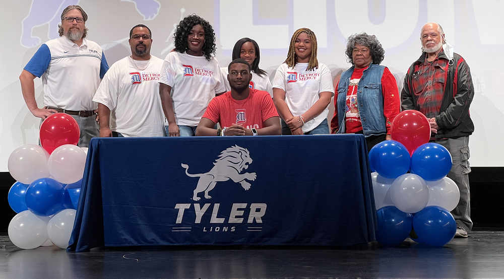Tyler High School senior Kendell Howard surrounded by his family as he sits at a table to sign letter of intent to play soccer in college