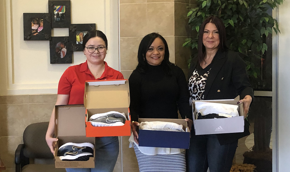 three women stand next to each other holding boxes of shoes