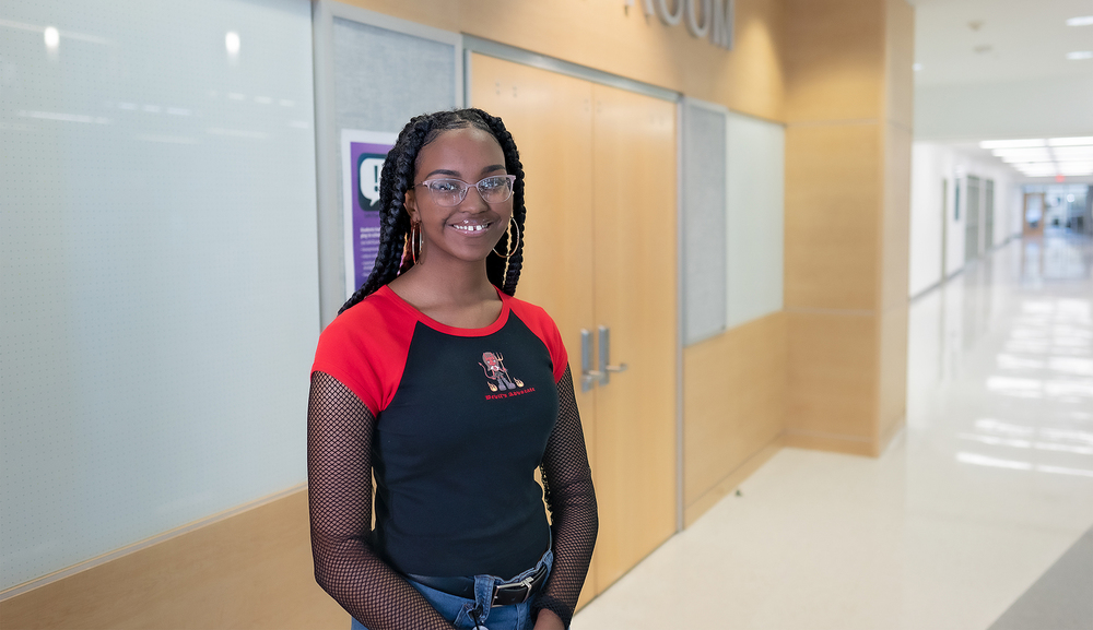 African American high school girl wearing red and black shirt stands in a hallway