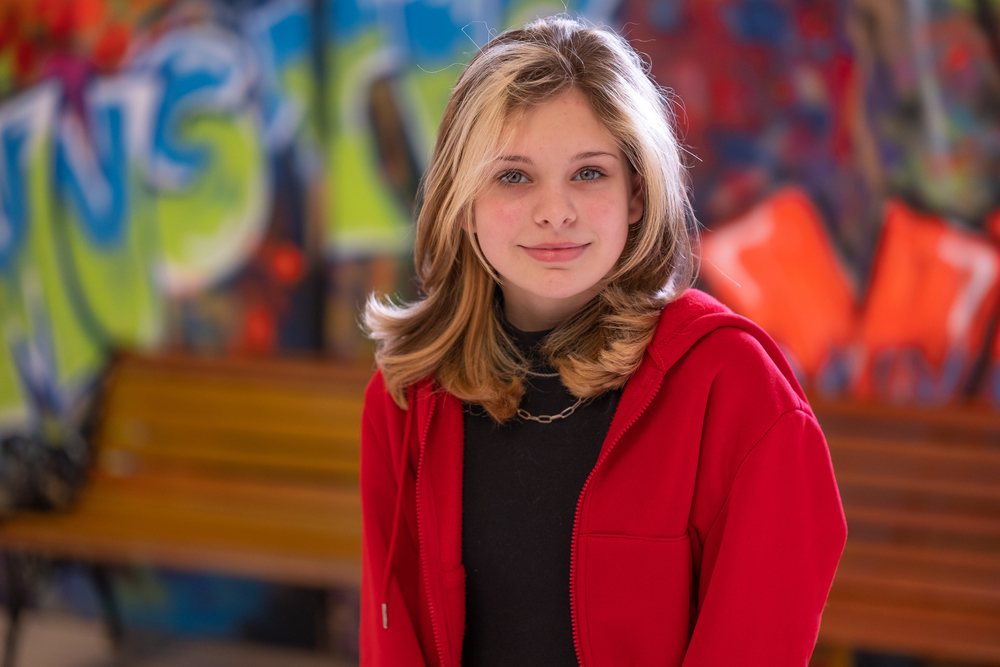 middle school age girl with blond hair wearing a black shirt and red sweater