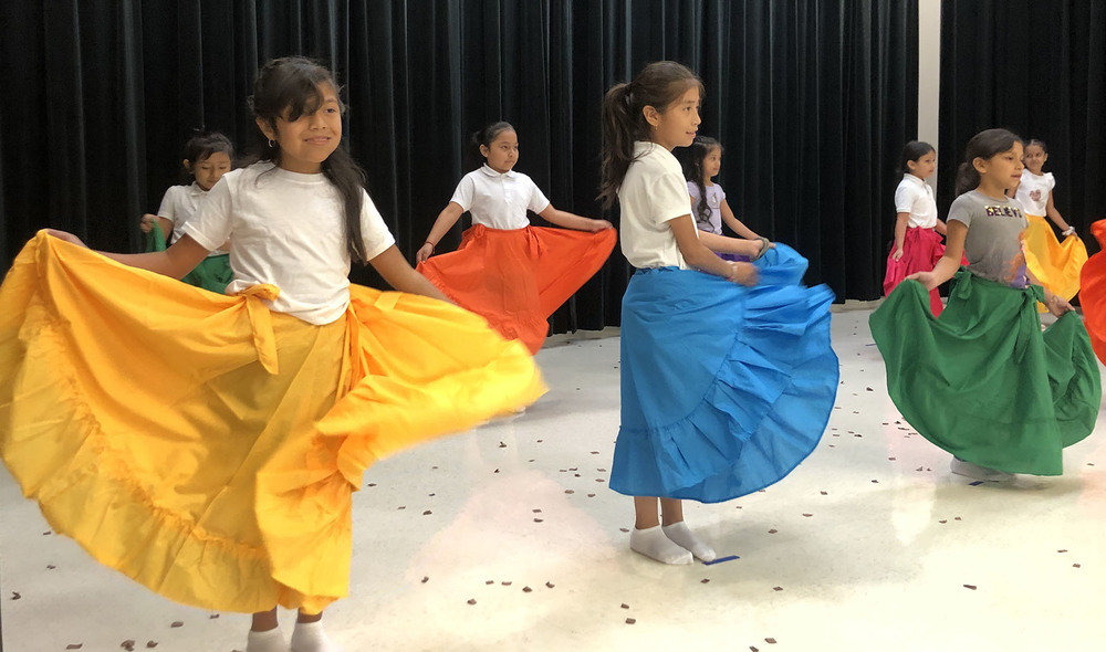 elementary aged girls wearing bright colored skirts and white shirts dancing