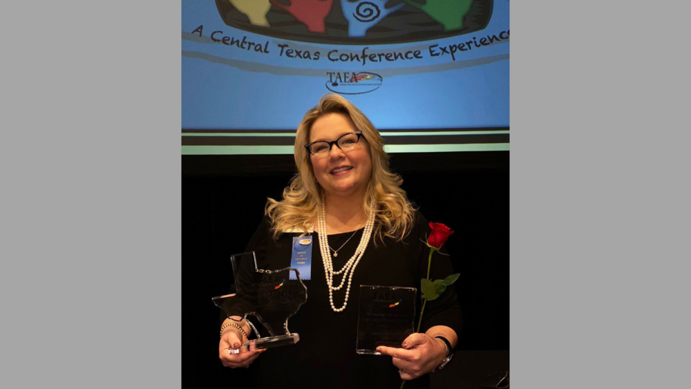 Sandra Newton holding two trophy/awards earned for being named administrator of the year by TAEA