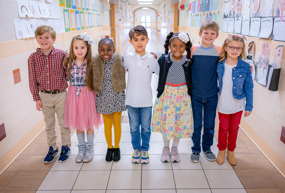 Elementary aged students standing in a row with their arms behind each others backs
