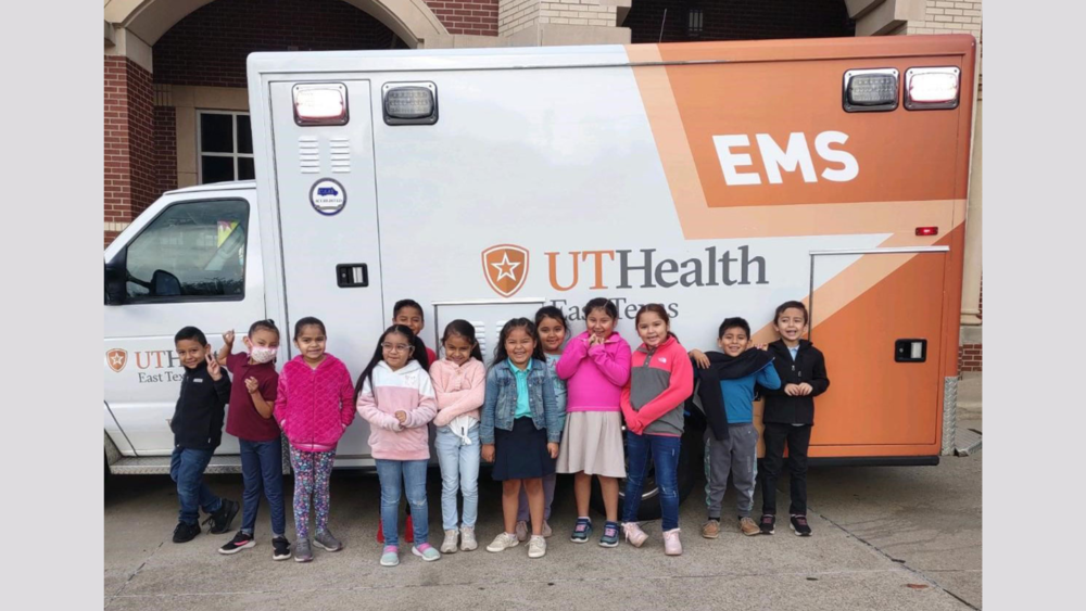 elementary aged students stand with a UT Health EMS ambulance behind them