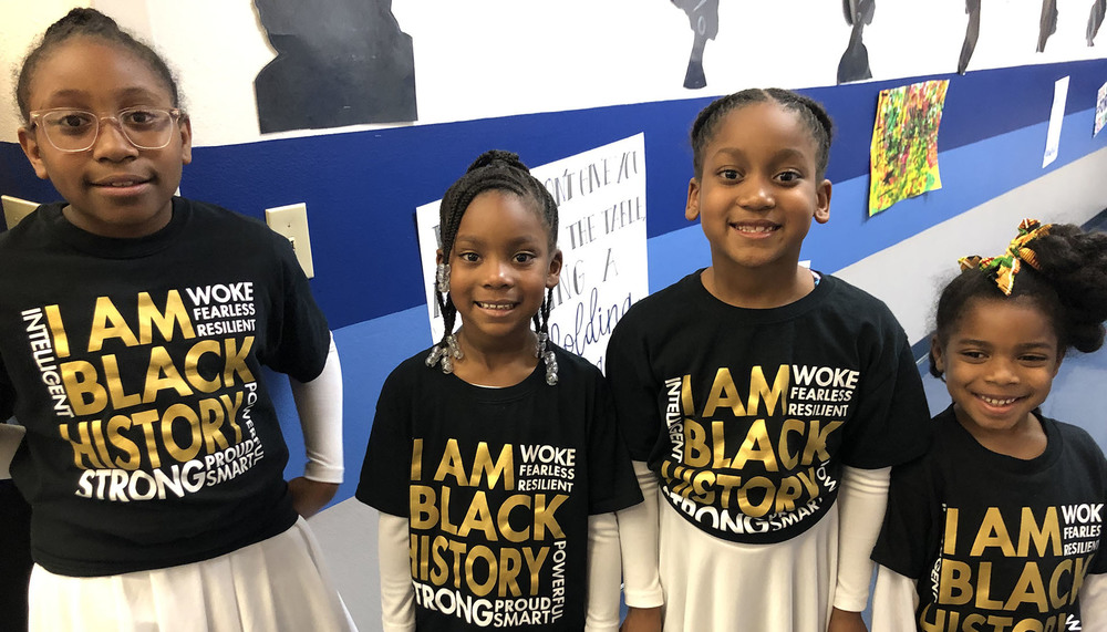 four elementary age African American children wearing black t-shirts that say, "I am Black History"