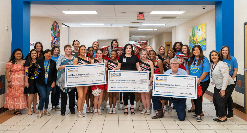 adults and cheerleaders standing in a hallway holding giant checks to surprise teachers with a grant
