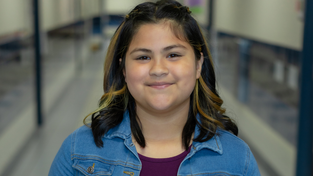 elementary age girl with brown shoulder length hair wearing a maroon shirt and denim jacket