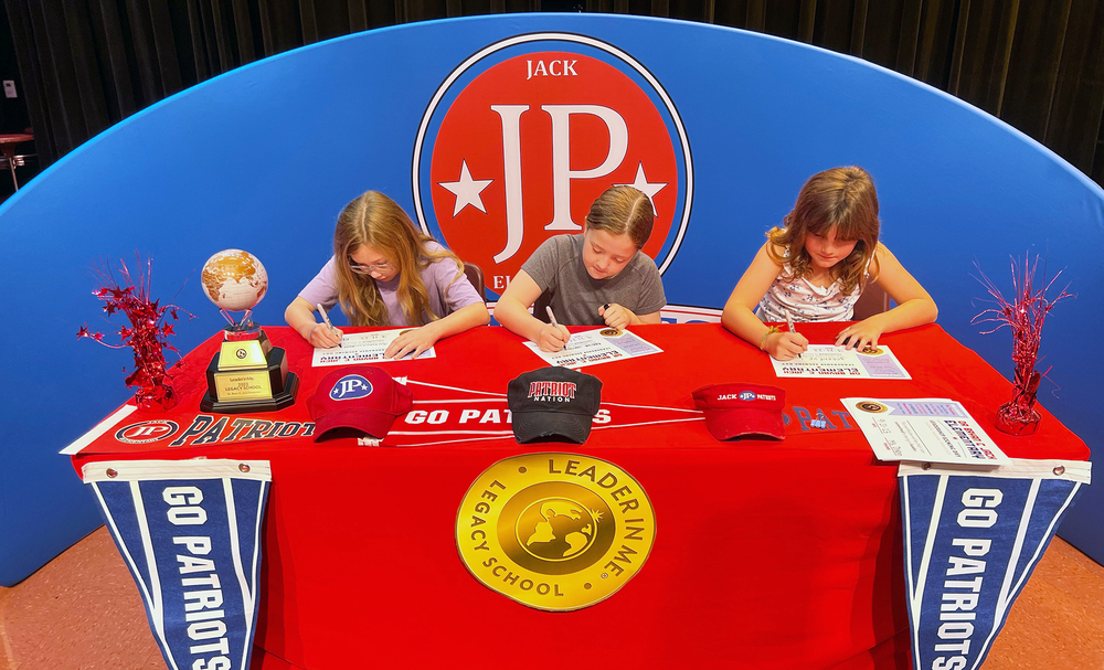 three elementary age girls sitting at a table signing papers
