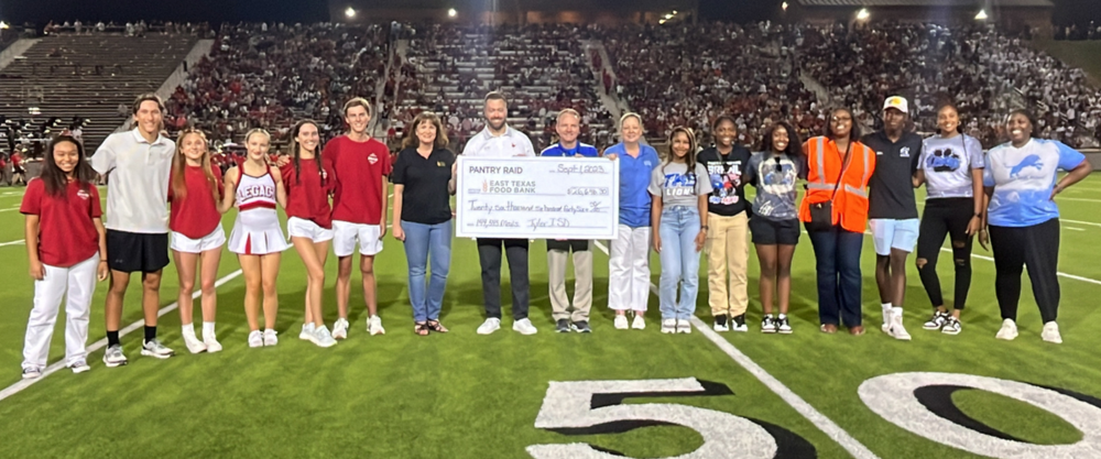 students and teachers on football field holding giant check