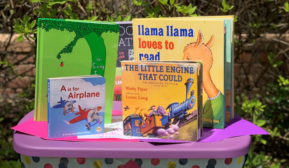 Books sitting on top of a polka dot tub with purple lid. The Giving Tree, Llama Llama Loves to Read, A is for Airplane and The Little Engine that Could