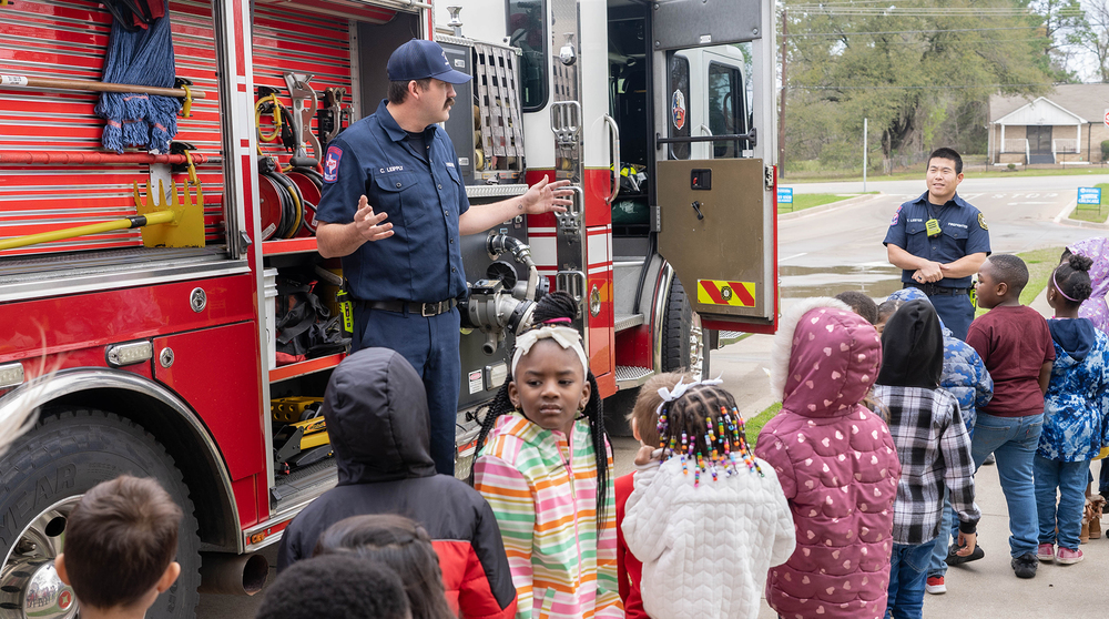 elementary age students standing beside a firetruck and fireman