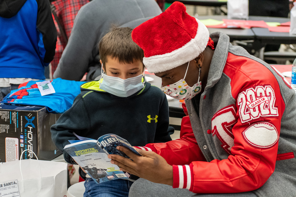Tyler Legacy football player reading a book to student.