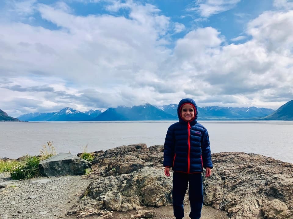 Boy smiles in front of lake and mountains in Alaska