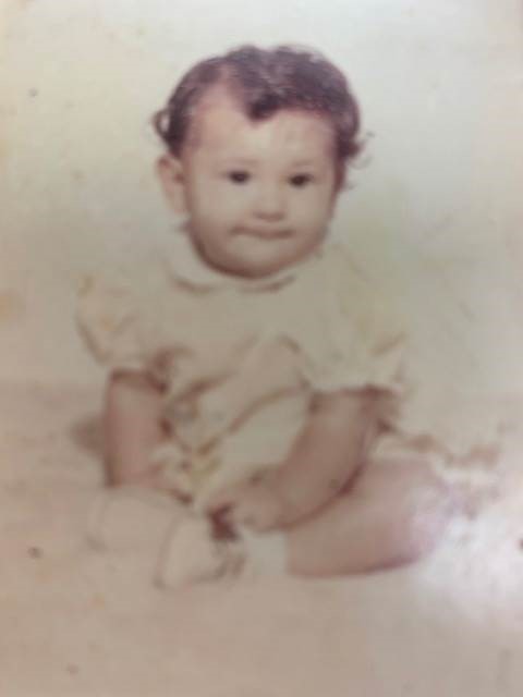 baby with curly short hair wearing a fluffy dress and smiling at the camera