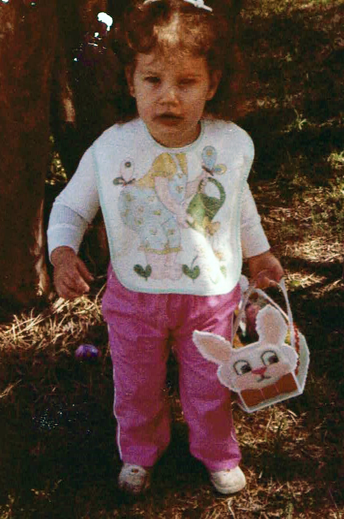 female toddler wearing pink pants and a bib, holding a bunny Easter basket