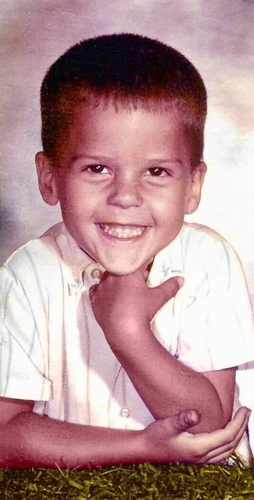 toddler boy smiling from ear to ear with his elbow on the table and hand under his chin
