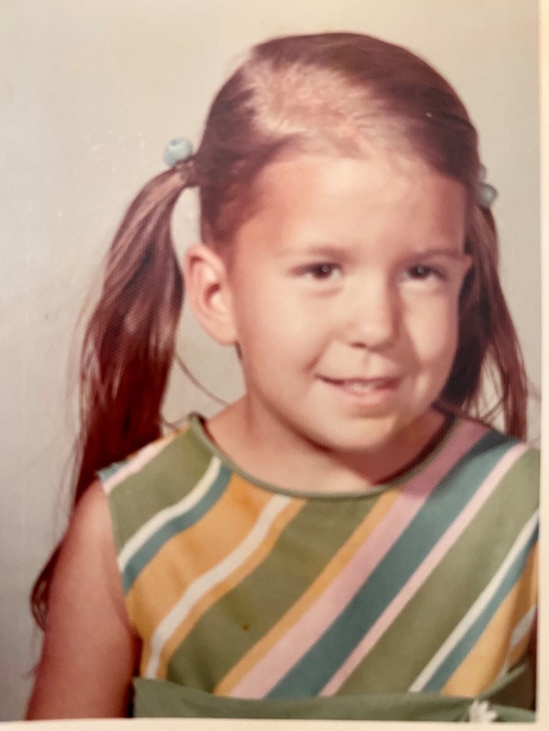 young girl with pigtails and a striped dress smiling at the camera