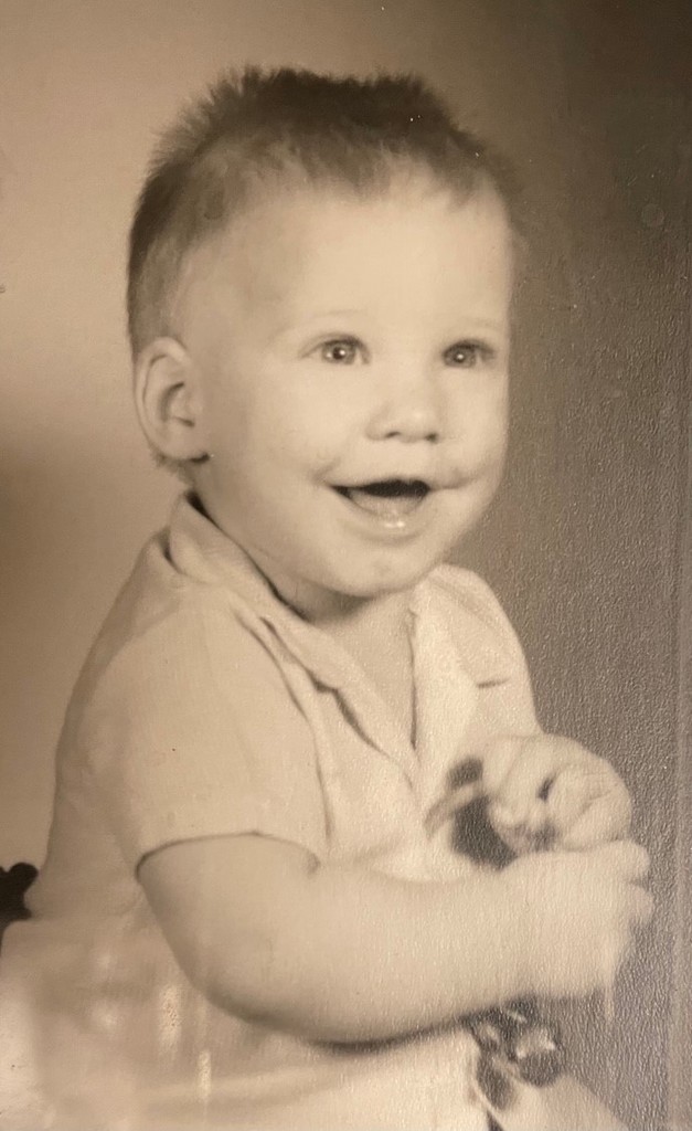 baby with short hair sticking up, smiling at the camera with mouth open and big eyes
