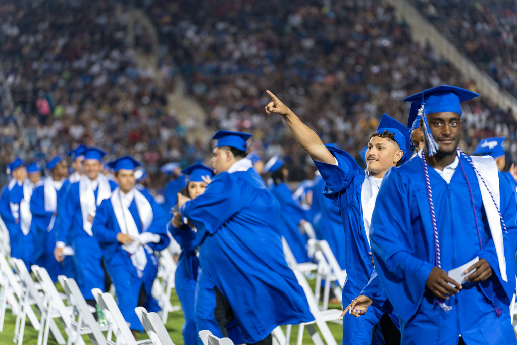 student walking and pointing towards crowd at graduation