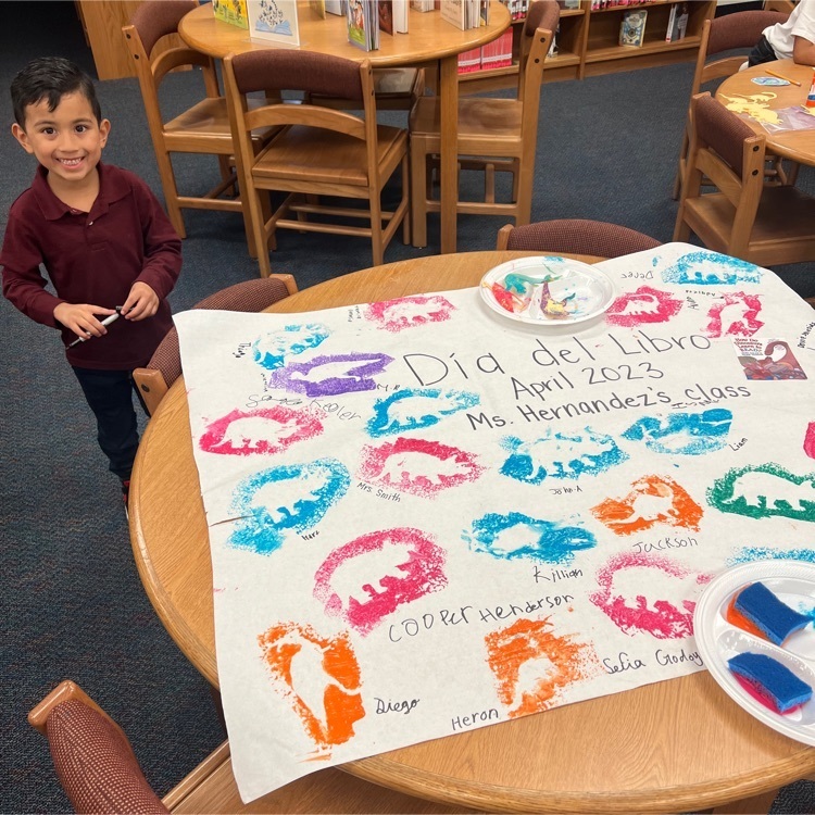A kindergarten student with their dinosaur mural during library class